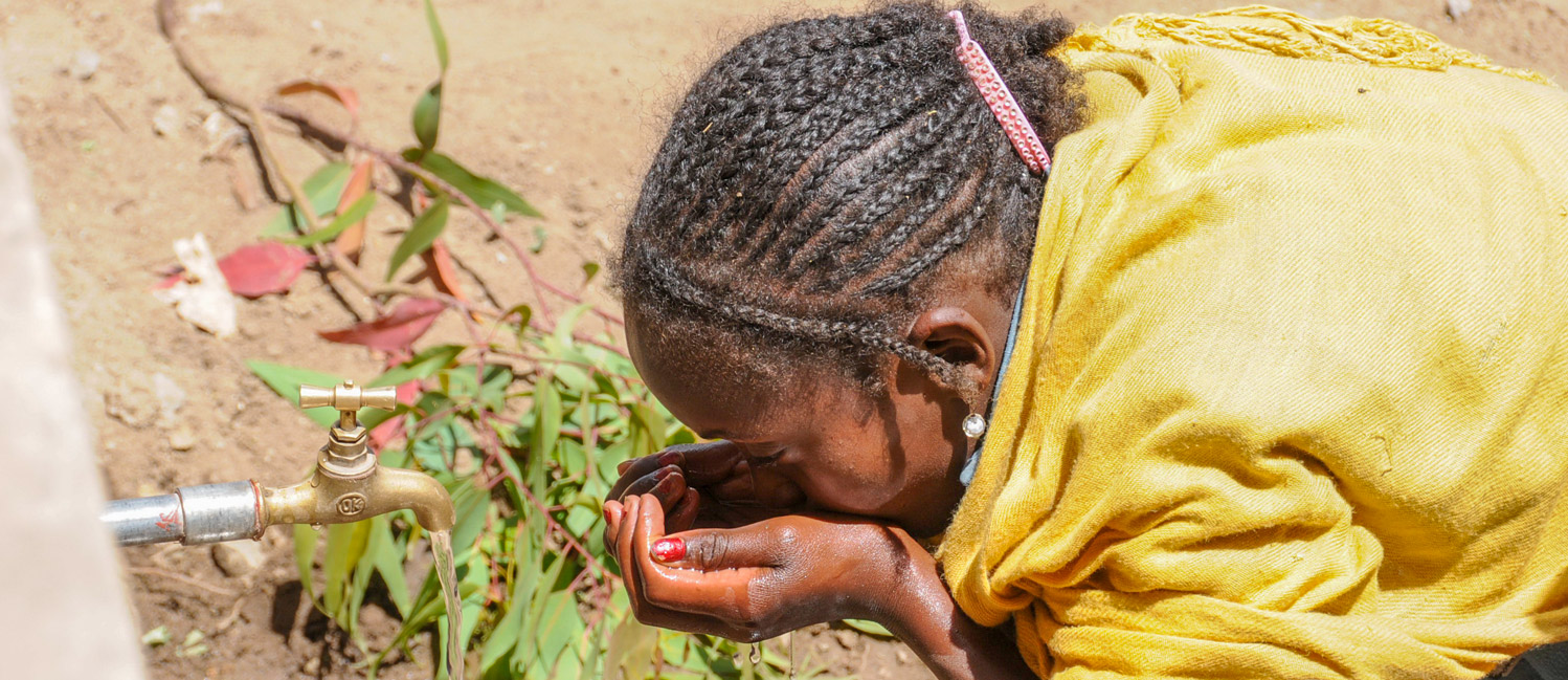 Bambina eritrea che beve l'acqua da un pozzo